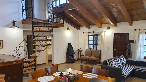 Un espacio habitable amplio con una mesa de comedor de madera, sillas, un sofá y una escalera con barandilla de hierro forjado.