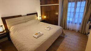 Una cama impecablemente arreglada con un edredón blanco acolchado, un cabecero de madera y una mesita de noche con lámpara.