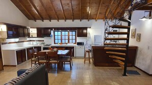 Una cocina amplia con vigas de madera, una zona de comedor con banco y una escalera con barandilla de metal.