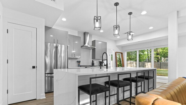 A modern kitchen with a central island, stainless steel appliances, and black bar stools.