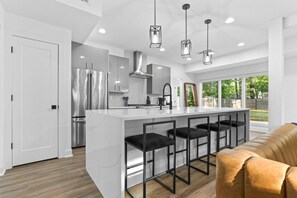 A modern kitchen with a central island, stainless steel appliances, and black bar stools. - Midtown Modern (Atlanta)
