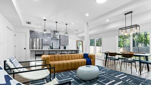 A modern living room with a sofa, round ottoman, and dining area with chairs and a table.