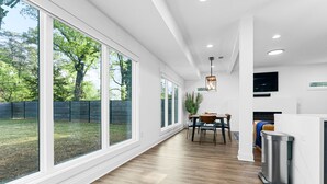 A modern kitchen with large windows, a dining area, and a trash can.