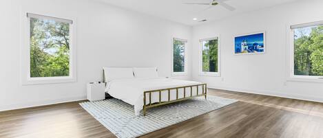 A spacious bedroom with a large bed, a ceiling fan, and multiple windows offering views of greenery.
