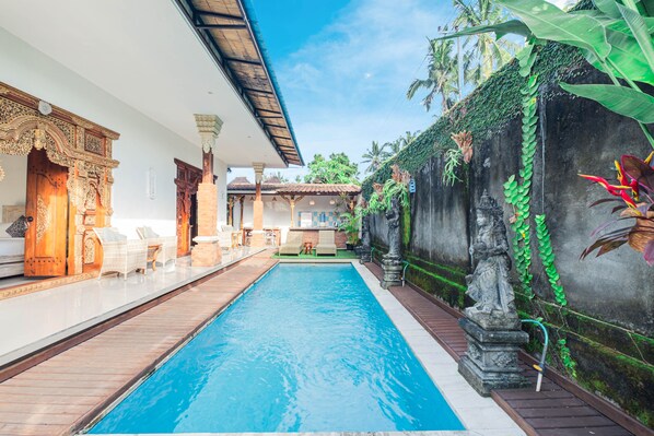 A swimming pool with a wooden deck, lounge chairs, and a stone statue.