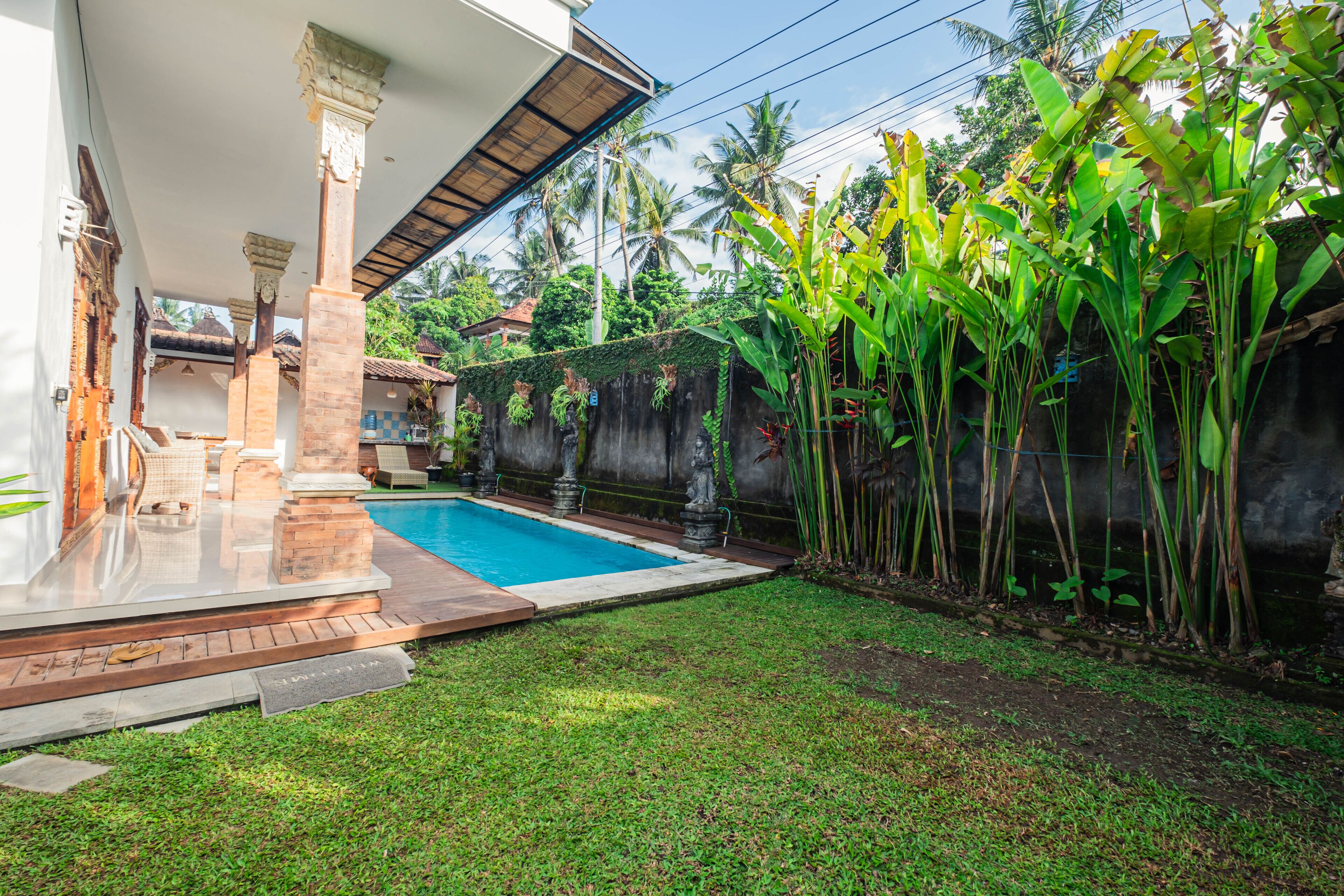 A swimming pool with a tiled deck, surrounded by a grassy area and a stone wall.