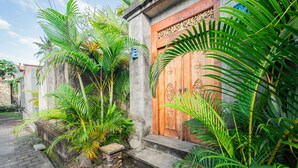 A traditional wooden door with intricate carvings, a concrete wall, and lush tropical plants. - Supala Private Living B (Ubud)