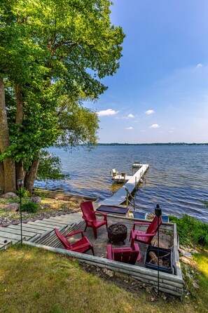A lakeside deck with red chairs, a table, and a dock extending into the water.
