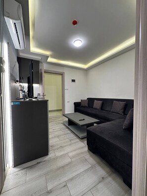 A modern living room with a sofa, a coffee table, a TV, and a built-in air conditioning unit.