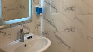A bathroom with a white sink, a mirror, and marble-patterned walls.