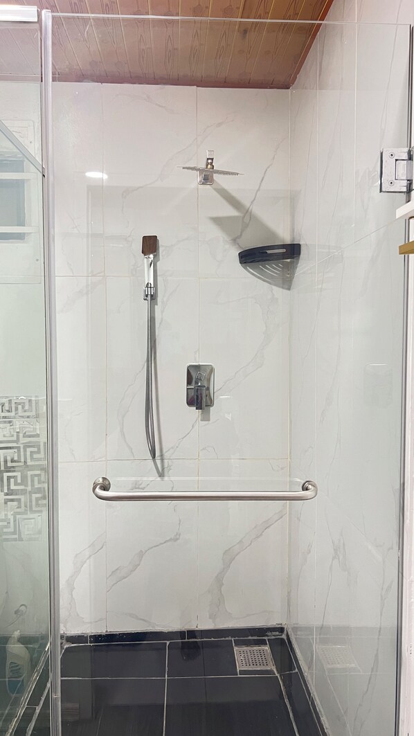 Une douche fermée par des parois en verre, dotée d’un pommeau de douche à main, d’un robinet mural et d’une brosse à main.
