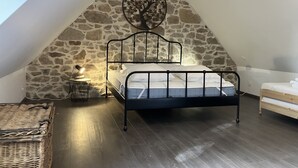 A bedroom with a sloped stone wall, a metal bed frame, a bedside lamp, and a small table with a lamp.