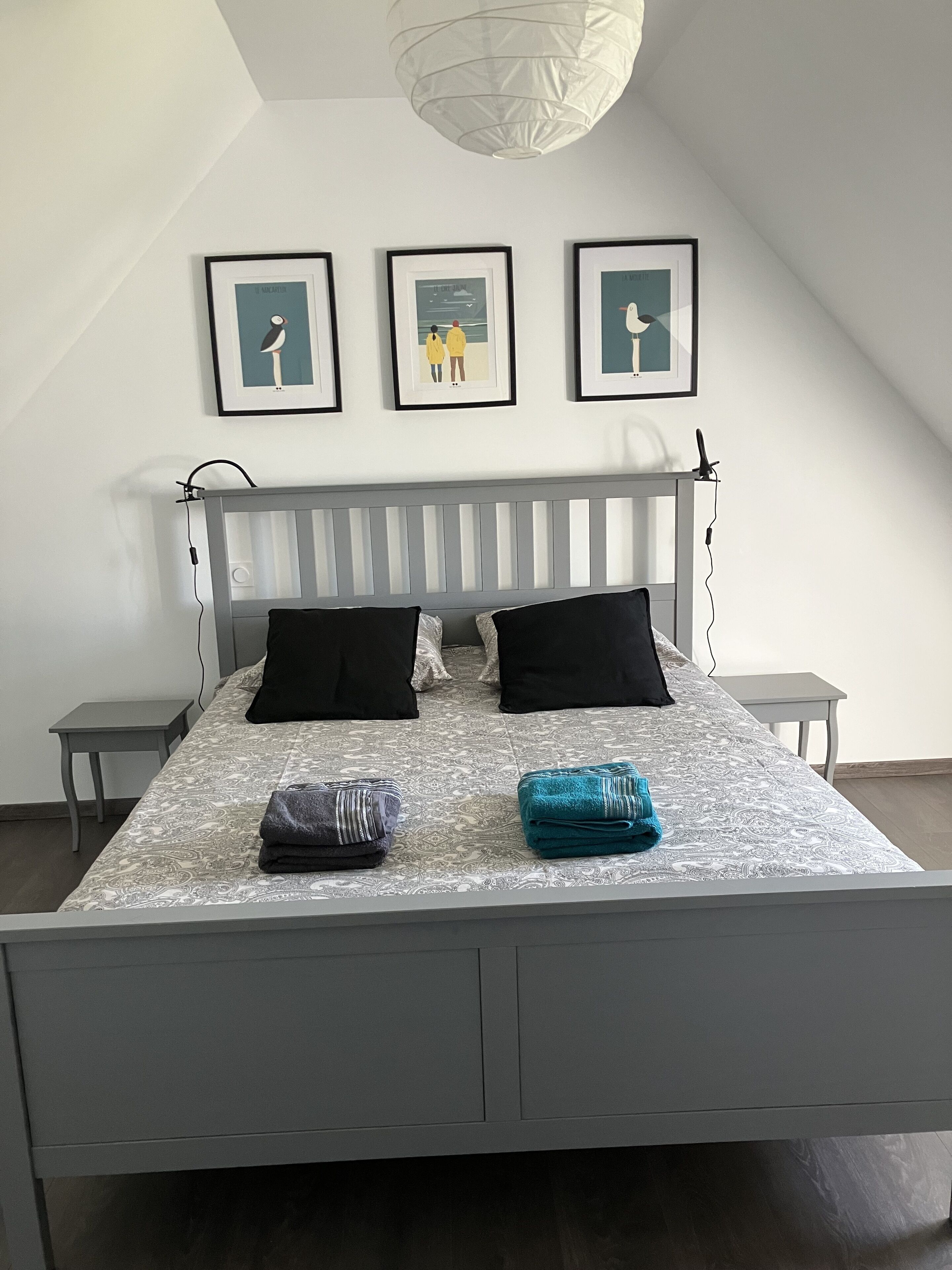 Een slaapkamer met een bed, twee nachtkastjes en drie ingelijste foto’s aan de muur.