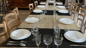 A long dining table set for a meal with chairs around it, a stone fireplace, and a wooden cabinet in the background.