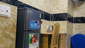 Una cocina compacta con salpicadero de mármol, un refrigerador negro, una mesa de comedor de madera y una silla azul.