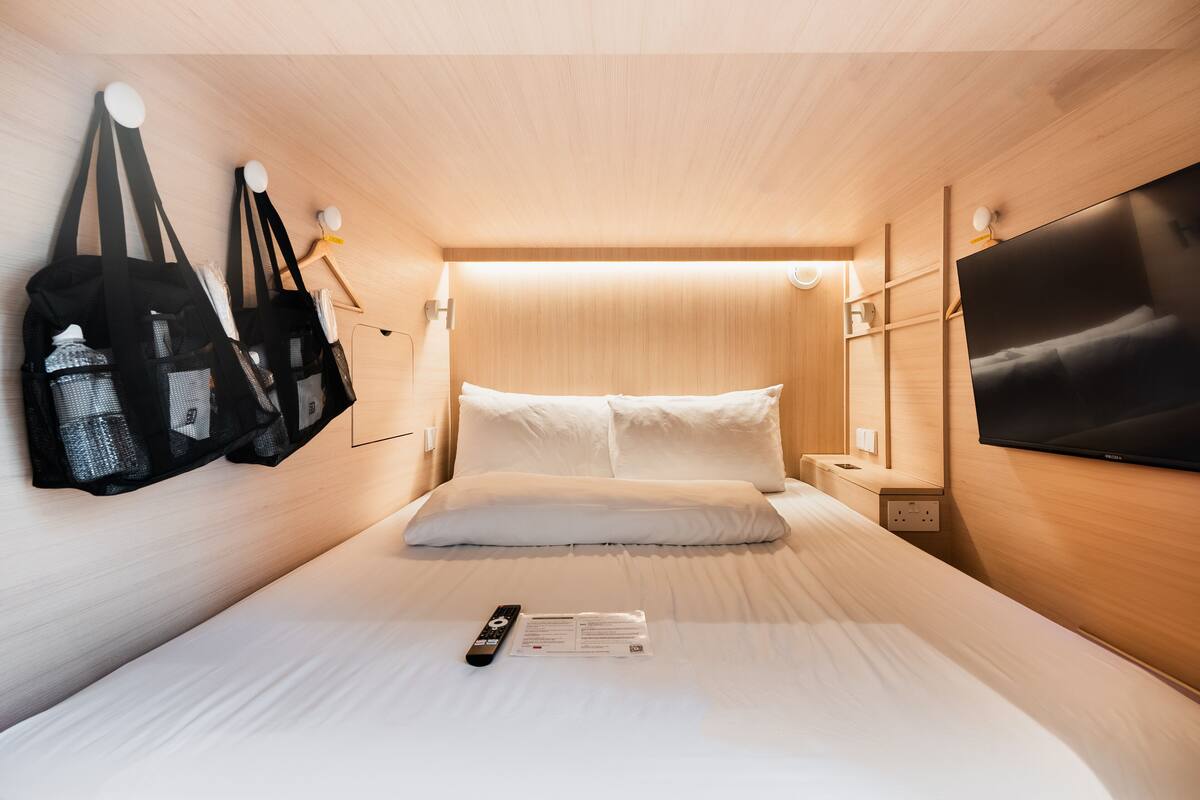 A compact hotel room with a bed, a TV, a bedside table, and a wall-mounted TV.