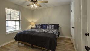 A bedroom with a bed, a ceiling fan, a window with blinds, and a door. - A Quiet Place - Home Away from Home Business Ready (Texarkana)