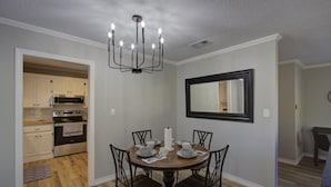 A dining area with a round wooden table, four chairs, a chandelier, and a large mirror on the wall. - A Quiet Place - Home Away from Home Business Ready (Texarkana)
