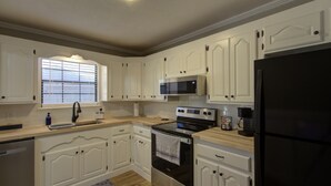 A kitchen with white cabinets, a black refrigerator, a microwave, an oven, and a coffee maker. - A Quiet Place - Home Away from Home Business Ready (Texarkana)