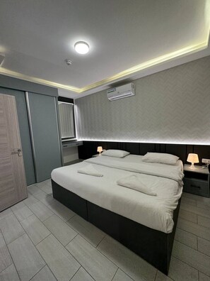 A modern bedroom with a large bed, bedside lamps, a ceiling light, and an air conditioning unit.