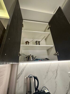 A kitchen with a built-in stove, a kettle, and a shelf with kitchen utensils.