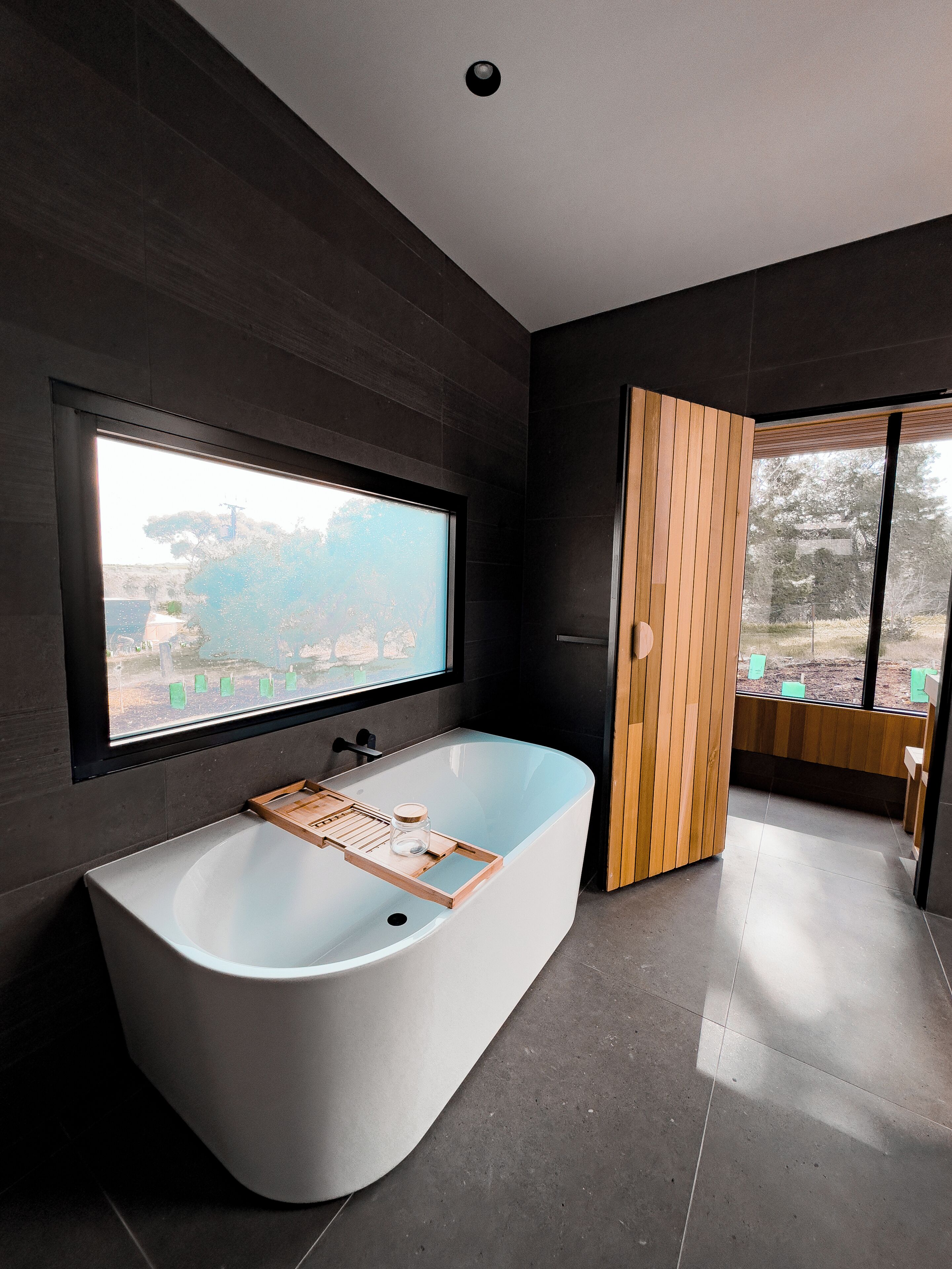 Ein modernes Badezimmer mit einer freistehenden Badewanne, einem großen Fenster und Ausblick ins Freie.