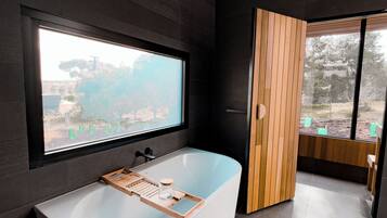 Ein modernes Badezimmer mit einer freistehenden Badewanne, einem großen Fenster und Ausblick ins Freie.