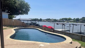 Una piscina con cubierta de madera y vistas a un muelle y casas al otro lado del agua.