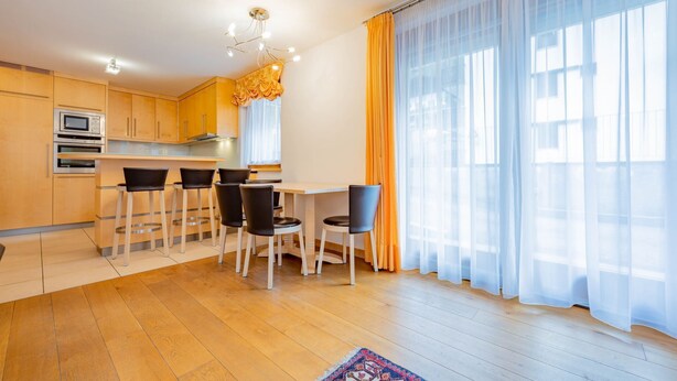 A modern kitchen with wooden cabinets, a built-in microwave, and a dining area with a table and chairs. - Beautiful and modern apartment in the center of Alba di Canazei (Canazei)