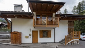 A two-story building with a wooden balcony, a front door, and a staircase leading to the upper floor. - Beautiful and modern apartment in the center of Alba di Canazei (Canazei)
