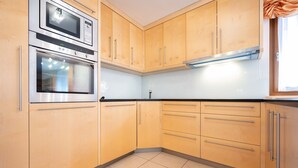 A kitchen with wooden cabinets, stainless steel appliances, and a tiled floor. - Beautiful and modern apartment in the center of Alba di Canazei (Canazei)