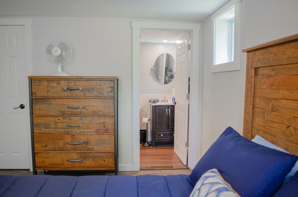 A bedroom with a wooden dresser, a bed with blue bedding, and a hallway leading to a bathroom.