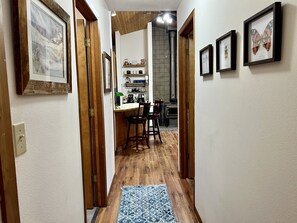 A narrow hallway with wooden flooring, a blue patterned rug, and framed pictures on the walls.