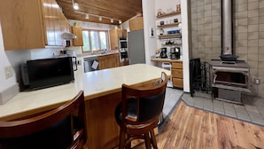 A modern kitchen with wooden cabinets, a central island, and a built-in oven. - The Ultimate Sunset on Flathead Lake (Polson)