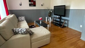 Un salón con un sofá beige, una mesita de centro, un televisor sobre un mueble bajo y un pequeño jarrón decorativo.