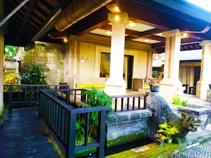 Relax in this serene outdoor space with a traditional architectural style, featuring columns, potted plants, and a stone lion statue.