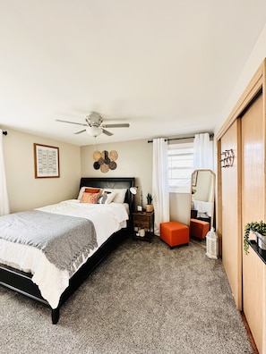 Ein Schlafzimmer mit Bett, Nachttisch, Spiegel, Deckenventilator und Kleiderschrank.