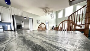 Una cocina con armarios blancos, un refrigerador de acero inoxidable, una encimera de mármol y una silla de madera.
