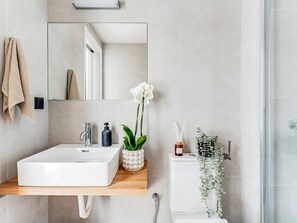 A modern bathroom with a white sink, a mirror, a towel rack, a toilet, and a shower area.