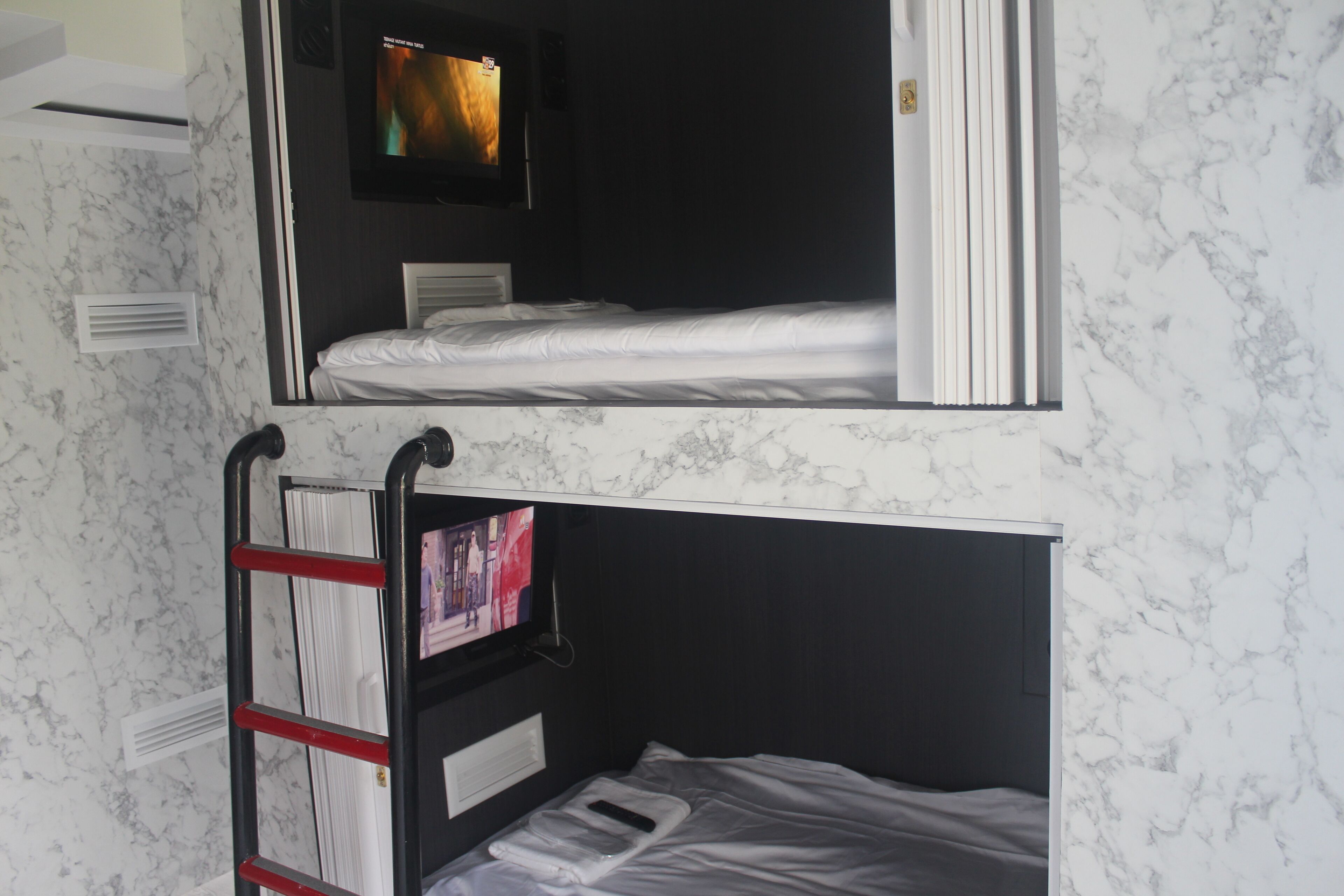 A room with a bunk bed, a TV mounted on the wall, and a ladder for the upper bunk.