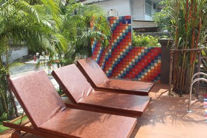 Three wooden lounge chairs with metal frames, a colorful tiled wall, and a small garden with palm trees. - H-District Boutique Poshotel (Bangkok)
