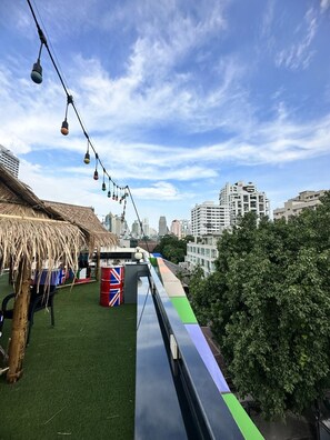 Une terrasse sur le toit, dotée d’un revêtement d’herbe artificielle, d’une structure à toit de chaume et offrant une vue sur le panorama urbain.