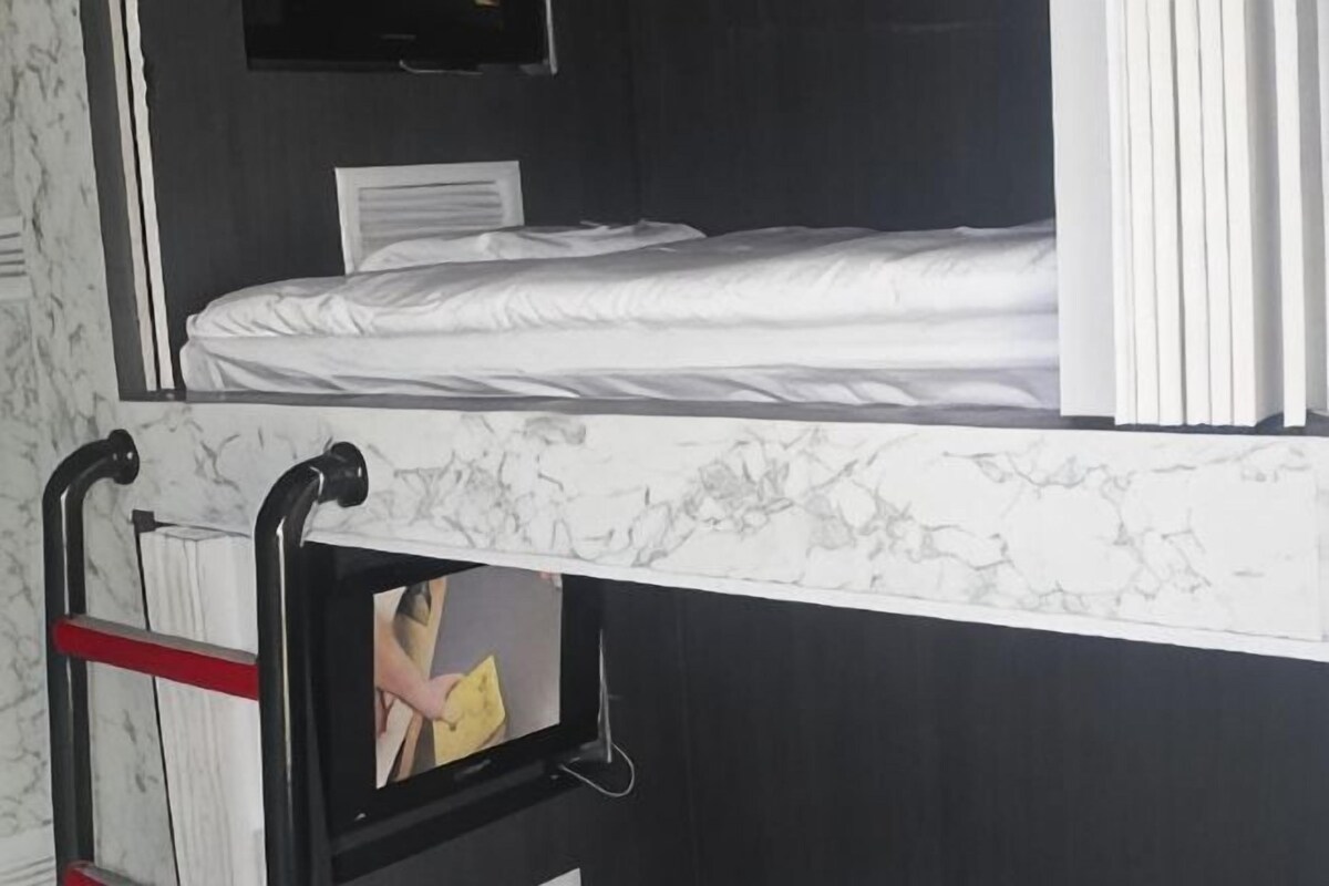 Een stapelbed met een witte matras, een zwart hoofdbord en een wandontwerp dat op marmer lijkt.
