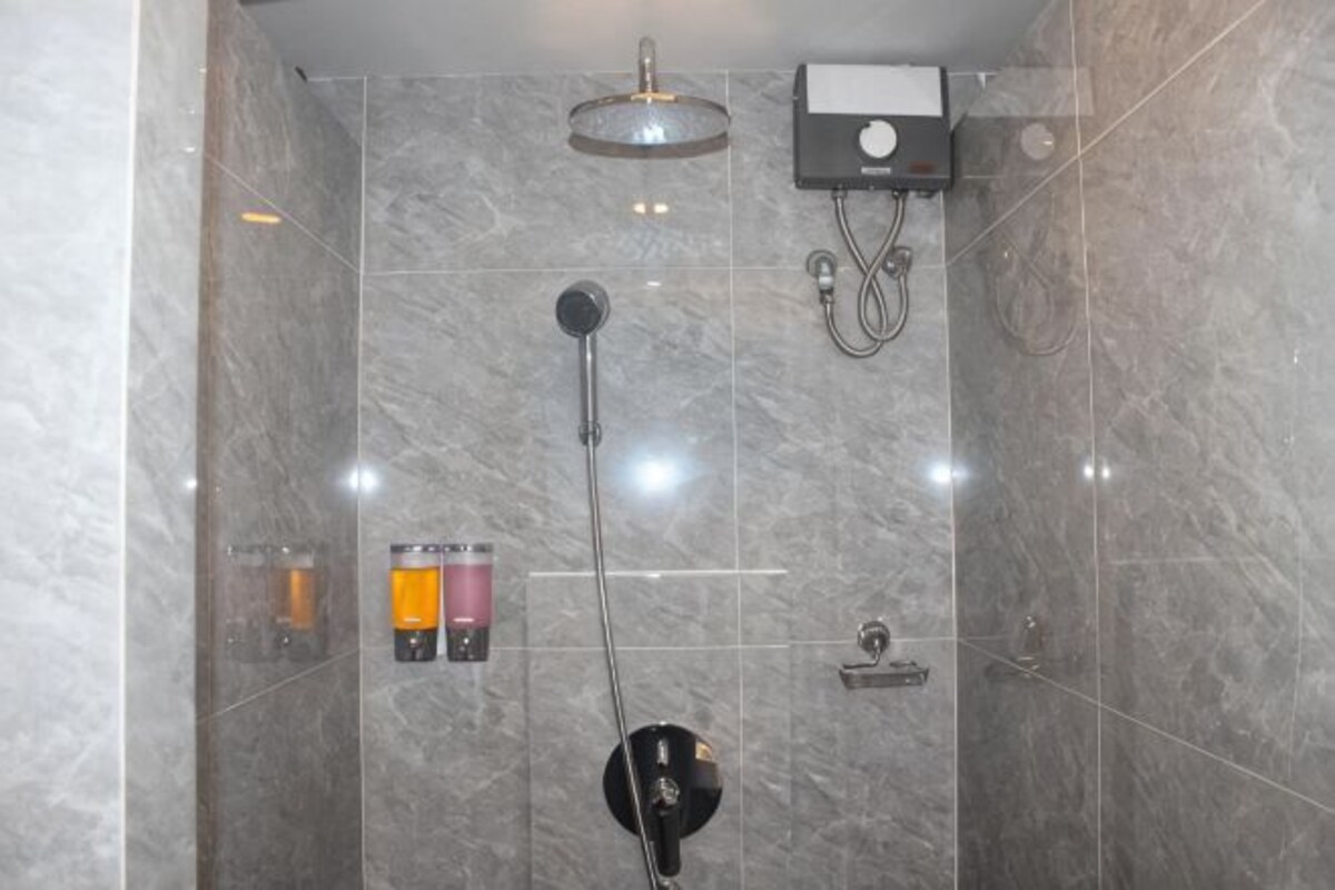 A shower with a handheld showerhead, a wall-mounted faucet, and a control panel.