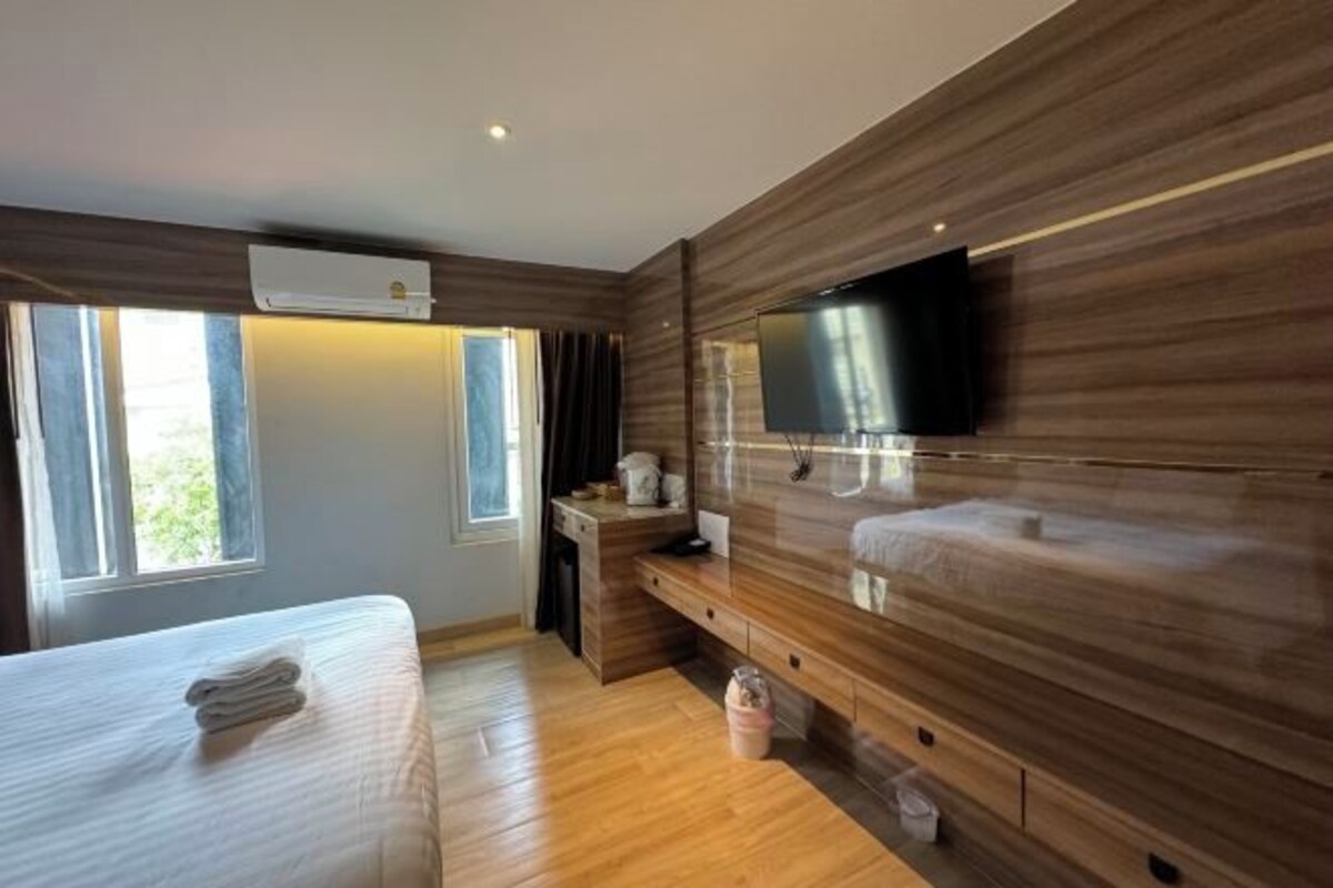 A modern hotel room with a wooden wall, a flat-screen TV, a desk, and a bed with a neatly folded towel.