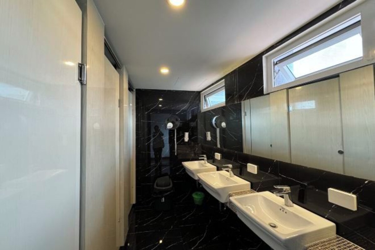 A modern bathroom with three sinks, a large mirror, and a toilet.