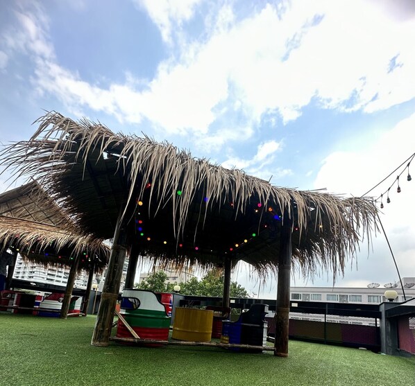 A thatched-roof structure with colorful lights, surrounded by green artificial grass, and a view of a building in the background. - H-District Boutique Poshotel (Bangkok)