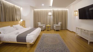 A modern hotel room with a large bed, two armchairs, a small table, a TV, and a patterned rug. - Seven Suites thimphu (Thimphu)