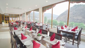 A dining area with tables set for meals, large windows offering a view of the mountains, and a modern interior design. - Seven Suites thimphu (Thimphu)