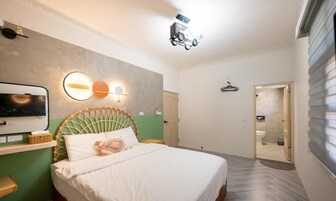 A modern hotel room with a bed, a television, a wall-mounted light fixture, and a door leading to a bathroom.